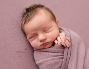 Newborn baby wrapped up with her hands showing