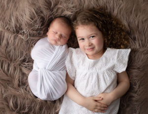 Big sister with her newborn brother laying on a flokati