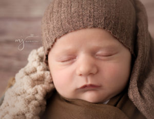 Newborn boy posed wrapped  in a metal bucket in our Rochester, NY studio.