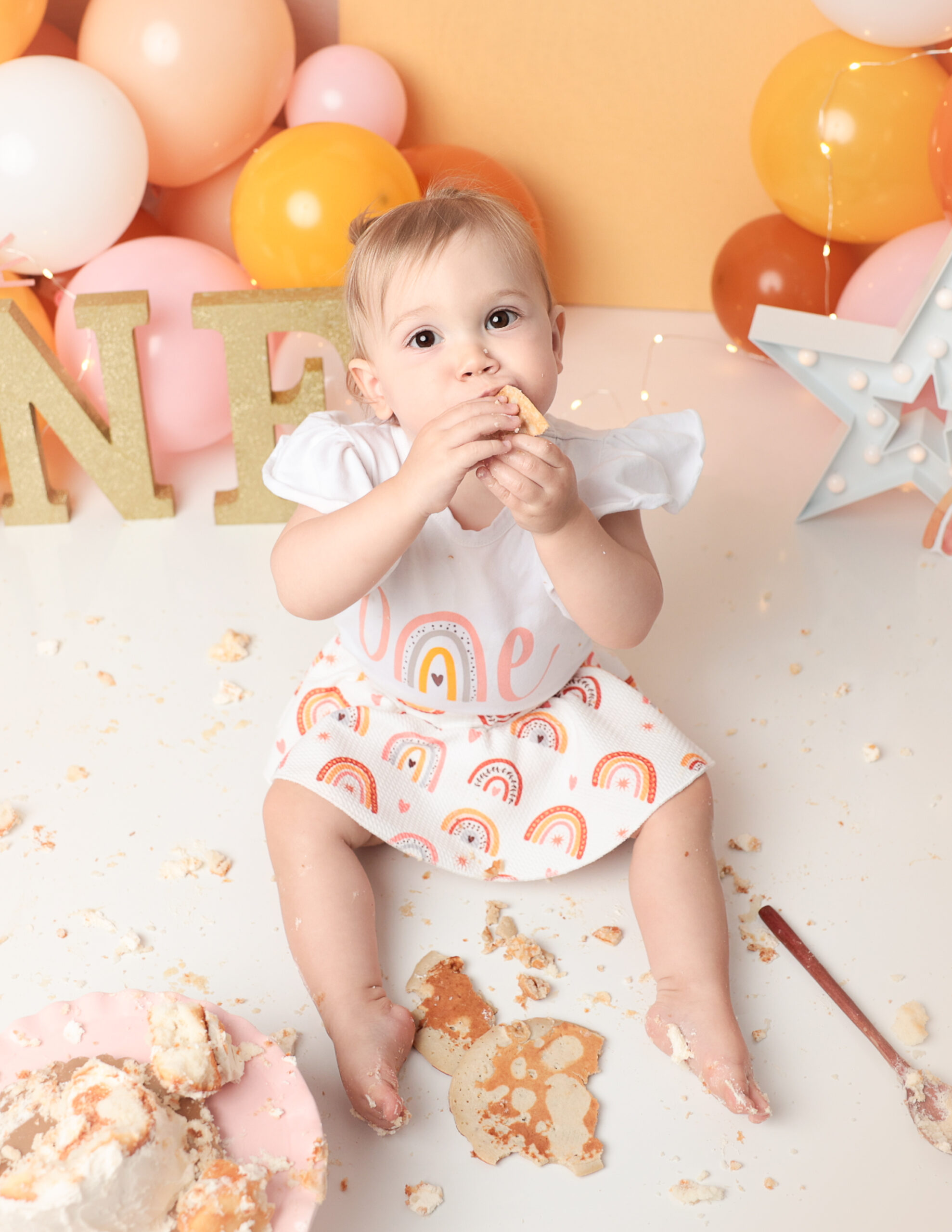 A joyful young girl surrounded by a vibrant boho-themed setup, celebrating her cake smash session at MJ Memories Photography studio in Rochester, NY.