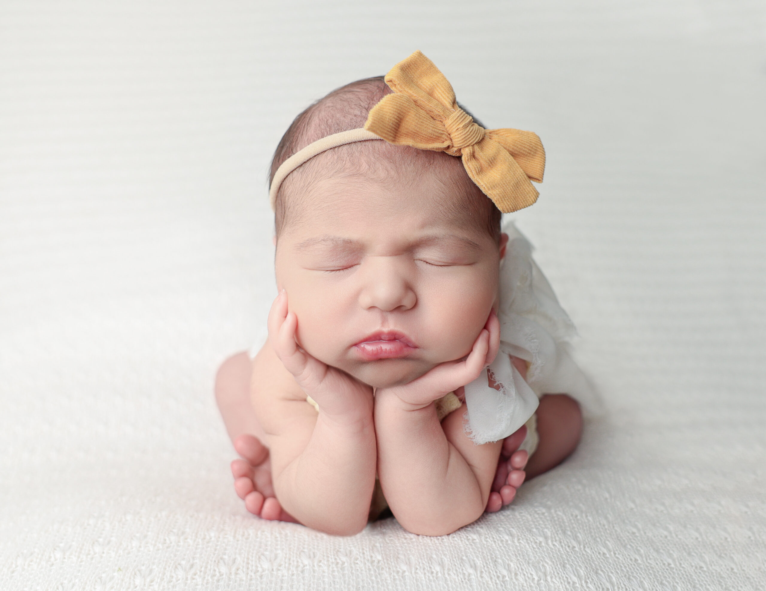 A newborn baby girl posed in a froggy position, showcasing her delicate features, tiny fingers, and toes taken in a cozy Rochester, NY photography studio.