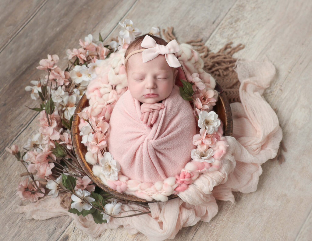 Newborn baby girl surrounded by floral decorations, captured during a photoshoot at MJ Memories Photography studio in Rochester, NY.