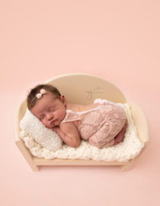 Baby girl in a ivory bed wearing a lace outfit and a bow headband at her newborn photography session 