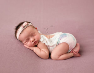 Infant girl wearing a romper laying on a pink backdrop