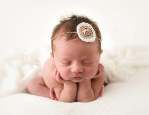 Baby girl in a froggy newborn pose on a white backdrop wearing a white headband