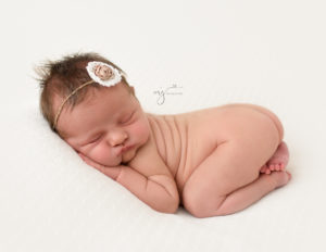 Newborn baby girl nude on a white backdrop wearing a headband at her newborn session