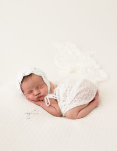 Newborn girl on a white backdrop with a bonnet and wrap on