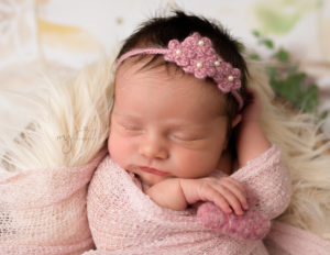 Baby girl sleeping holding a heart and wrapped up with a pink flower headband on