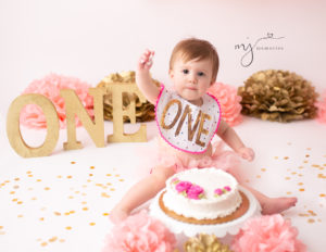 Baby girl wearing a ONE bib holding up her cake smash cake