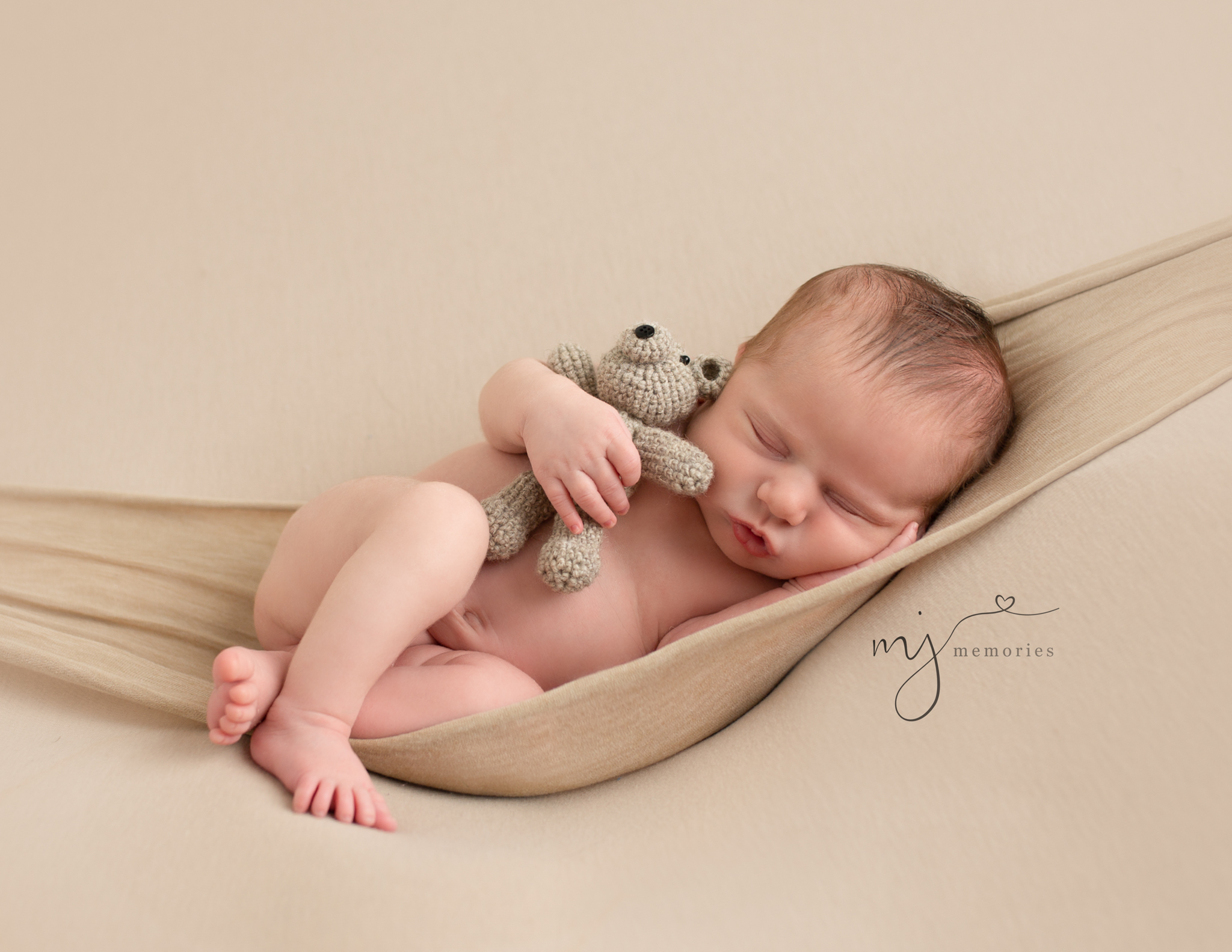 Newborn baby laying in "hammock" holding a tiny teddy bear