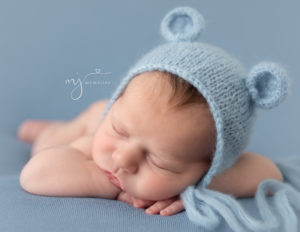 Infant boy in head on hands pose wearing a blue bear bonnet