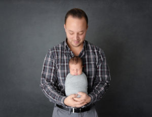 Dad posed with newborn son at our in-home Rochester, NY studio.