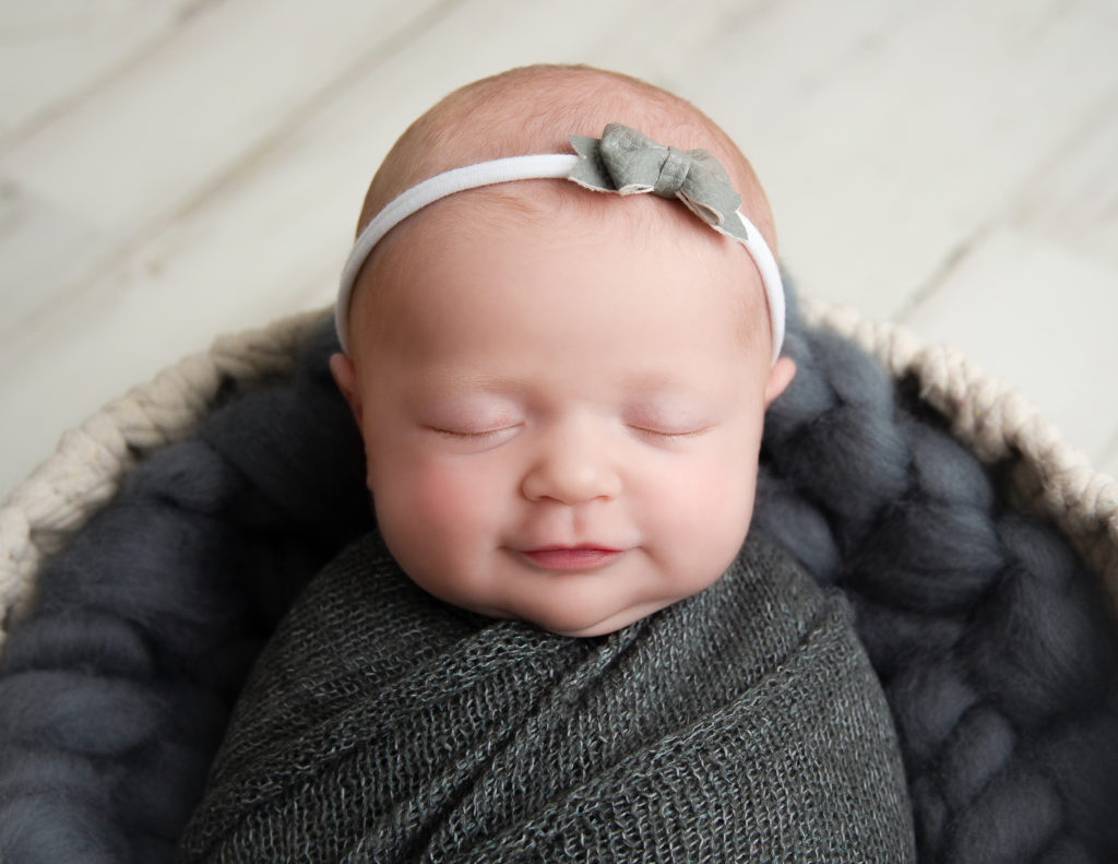 Smirking newborn girl posed at our Rochester, NY studio.